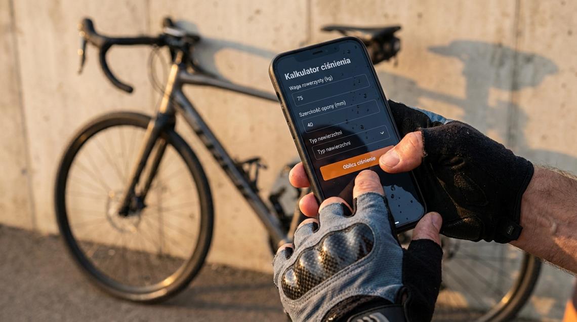 Rowerzysta obsługujący kalkulator ciśnienia opon na smartfonie z widokiem na nowoczesny rower gravelowy.